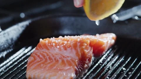 Close up view of A chef's hand squeezes a fresh lemon over a peace of sea fis Stock Footage 265839859