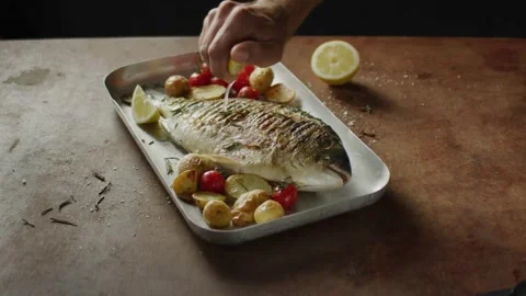 Close up view of A chef's hand squeezes a fresh lemon over a peace of sea fish. Stock-Footage 336588596
