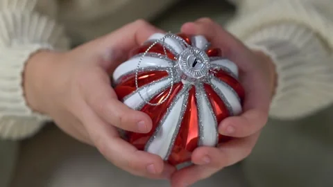 Close-up view of child hands gently holding red white Christmas ornament, warm Video stock 322195674