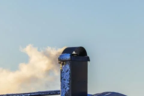 Close up view of chimney pipe releasing smoke into cold winter air above roof. Fotos Stock