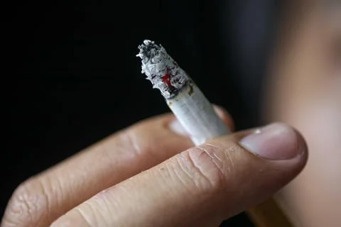 Close up view of a cigarette being held by someone with two fingers. Stock Photos