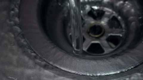 Close up view of clear fresh water running down plug hole in metal sink Stock Footage 104783833