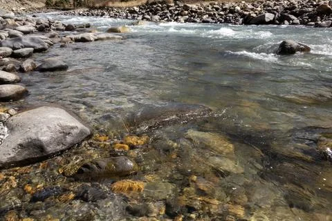 Close up view of clear river with sunlight reflecting on colorful stones an.. Stock Photos