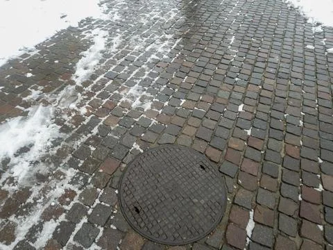 A close-up view of a cobblestone pavement covered in snow, featuring a circular Stock Photos