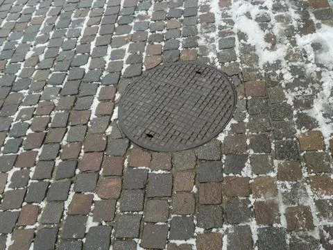 A close-up view of a cobblestone surface featuring an iron manhole cover amid Stock Photos