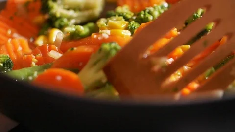 Close up view of colorful steaming vegetables frying on a pan being mixed and Stock-Footage 107381433