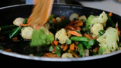 Close up view of colorful steaming vegetables frying on a pan being mixed and to Stock Footage 157753231