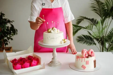 Close up view of confectioner decorating cake, pink colored pastry, capcakes and Stock Photos