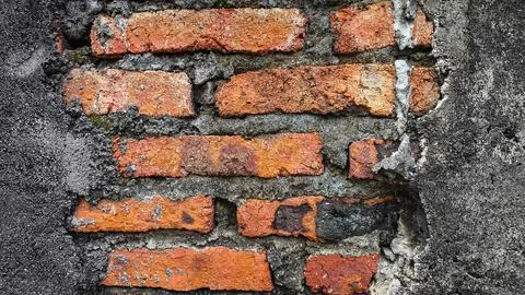 Close-up view of cracked red brick wall joined by rough concrete seam. Rust.. Stock Photos