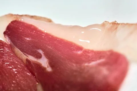 Close-up view of cured ham slice with fat layer on white background Фото