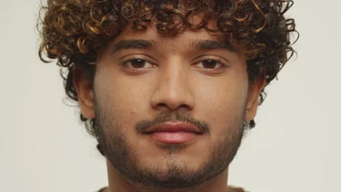 Close up view of a curly young man blinking with slight smile. Cheerful male Stock Footage 231568837
