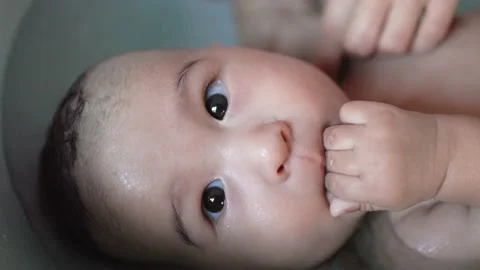 Close up view of Cute baby having bath and sucking his fingers. Mother holds and Stock Footage 204072469