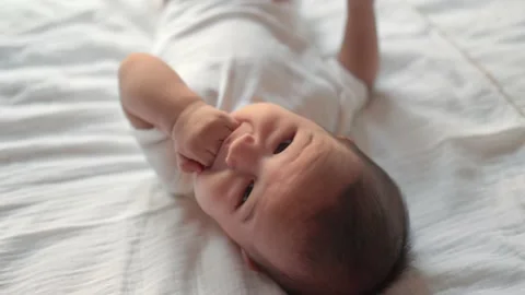 Close up view of Cute baby put fingers into mouth while lying on bed Stock Footage 202072423