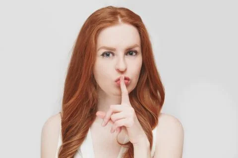 Close up view of cute ginger young woman, holding a finger on her lips, saying Stock Photos