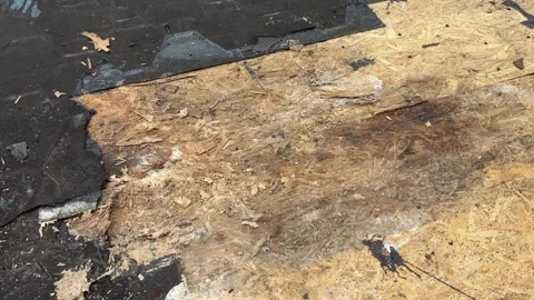 Close view of damaged asphalt shingles and exposed plywood decking during roof Stock Footage 346757058
