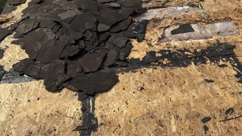 Close view of damaged asphalt shingles and exposed plywood roof deck during Stock Footage 346757165