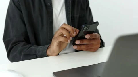 Close up view of dark skinned man sitting at the white table using smart phone Stock Footage 196127068