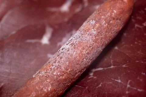 Close-up view of a delicious dry cured sausage resting on cured meat slices Stock Photos
