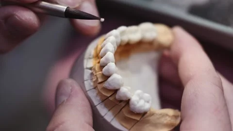 Close up view of dental technician draws white ceramics glaze on prosthesis of Stock Footage 136026384