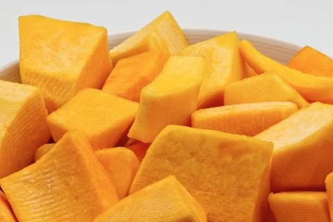 A close-up view of diced pumpkin pieces in a white bowl. Stock-Fotos