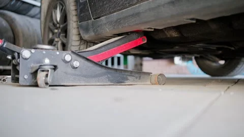 Close-up view of a dirty black car being raised by a hydraulic floor jack in a Stock Footage 339273815