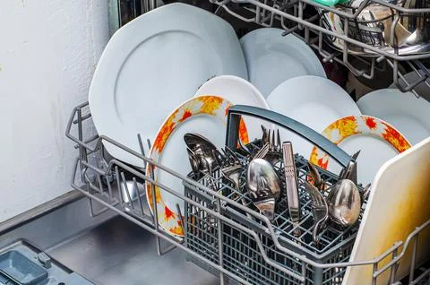 A close-up view of a dishwasher rack filled with clean white plates and sil.. Stock Photos