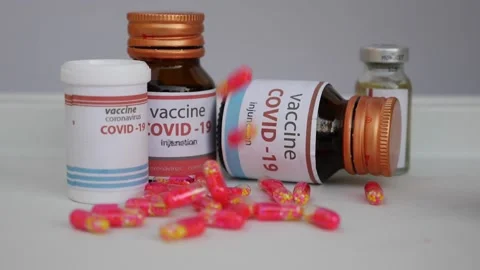 Close view of dropping capsules in front of covid-19 vaccine bottles 動画素材 147697196