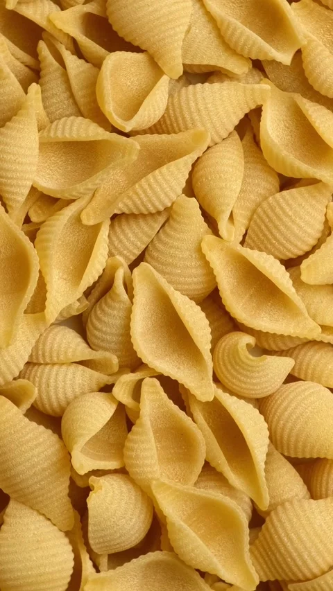 Close-up view of dry conchiglie pasta spinning. Uncooked Italian shell macaroni Stock Footage 344993148
