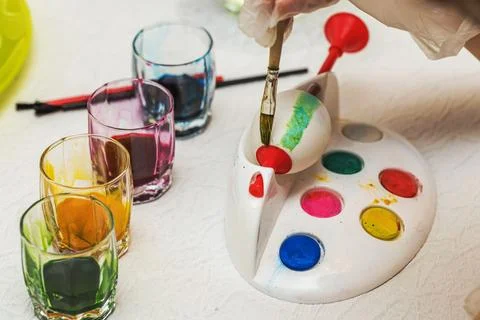 Close-up view of Easter egg painting process with colorful paints and brushes 스톡 사진
