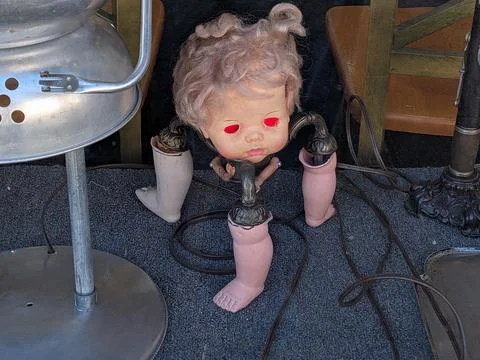 Close view of eerie doll head sculpture with metal body and three legs Stock Photos