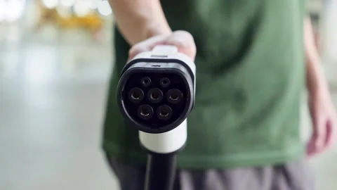 Close-up view of an EV charging plug held forward by a person in a green shirt Stock Footage 314770793