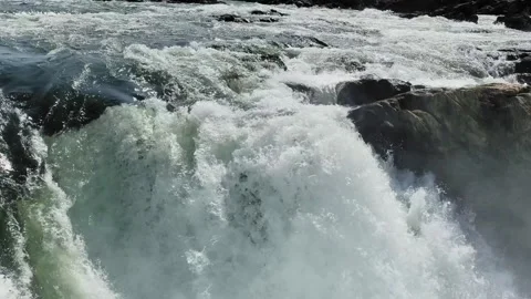Close view of fast-moving waterfall water crashing over dark rocks, creating Видео 331280539