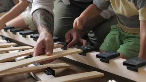 Close up view of father with kids assembling wooden slats of an orthopedic base Stock Footage 248309880
