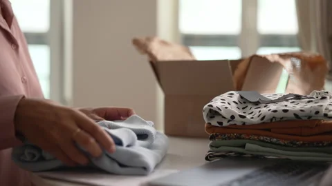 Close view of female freelancer using laptop and putting clothes in box at table Stock Footage 171097830