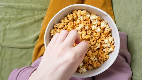 Close up view on female hand holding and eating a popcorn while watching a movie Stock Footage 200029477