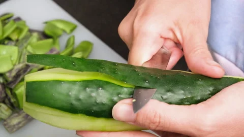 Close up view of female hands peeling a cucumber with a vegetable peeler Stock Footage 280802369