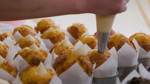 Close-up view of female hands puts the cream from pastry bag on cupcakes. Stock Footage 109473284