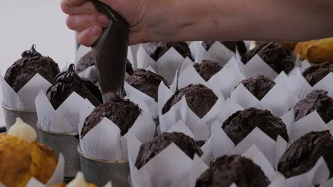Close-up view of female hands puts the cream from pastry bag on cupcakes. Video stock 109473331