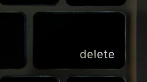 Close view of a finger pressing the Delete key on a laptop keyboard in a dark Видео 333982098