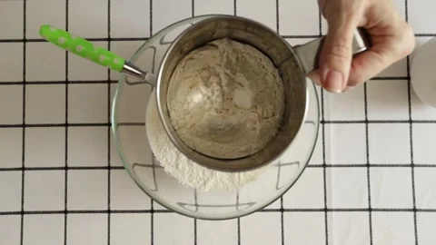 Close-up view of flour being sifted into a glass bowl with a sieve during h.. Stock Footage 315973702