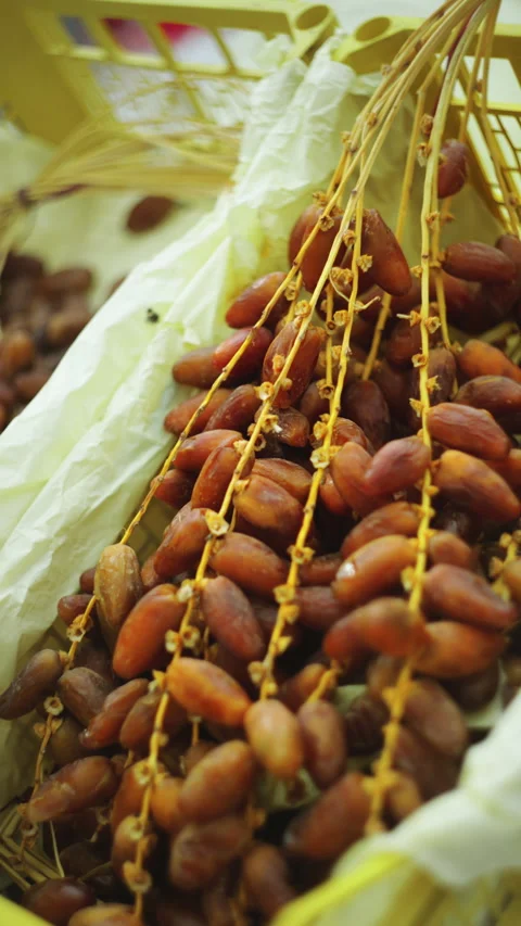 Close-up view of fresh brown dates on stalks in a yellow crate at an outdoo.. Video stock 329132733