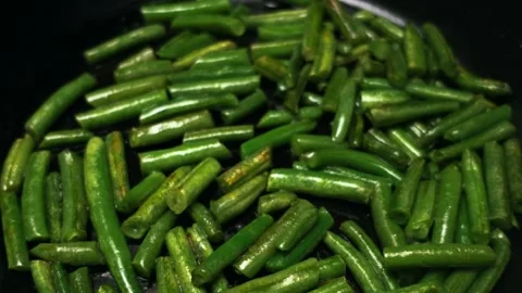 Close-up view of fresh green beans being sautéed in a dark pan with oil Stock Footage 338431958