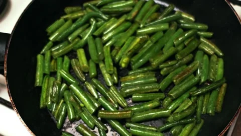 Close-up view of fresh green beans being sautéed in a black frying pan on a Stock Footage 338431961