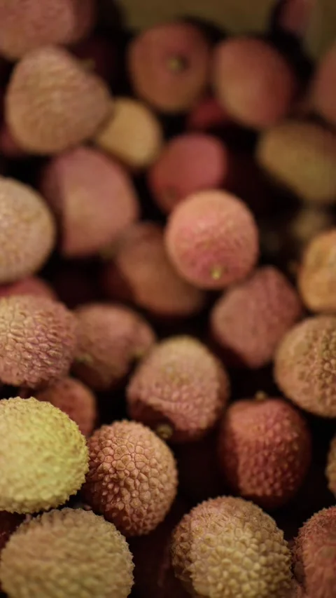 A close-up view of fresh lychee fruits with textured pink and yellow skin, piled Video stock 295879599