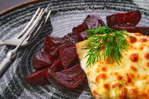 Close up view fried cod fillet with melted cheese topping and roasted beetroo Stock Photos