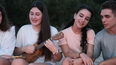 Close view of friends sitting around bonfire, playing ukulele on sandy beach Stock Footage 167298760