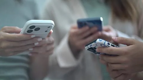 Close-up view of friends using mobile devices together, focused on hands and  Stock Photos