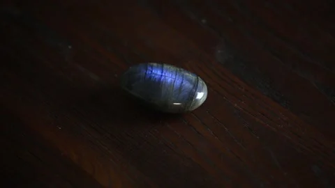Close up view of gemstone labradorite spinning on brown wooden background. Video stock 147345644