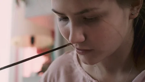 Close up view of gilr's face chewing a top of painting brush. Concentration Stock Footage 130122979