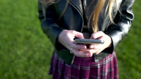 Close-up view of girl using mobile phone at park, Lather jacket, skirt Stockbeeldmateriaal 231915727